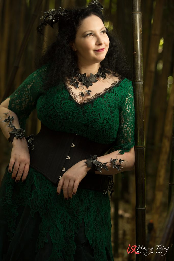 Melian, dark forest nymph, with a leafy green lace gown, black silk corset and black and silver leaves, crystals and horns.